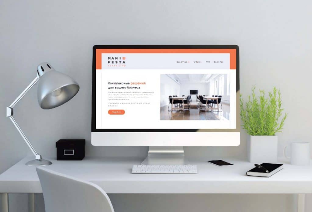 На столі стоїть комп'ютер з великим екраном, на якому відкрито веб-сайт із презентацією комерційного простору. Біля монітора розташовані настільна лампа, квітка у вазі та канцелярські приладдя.